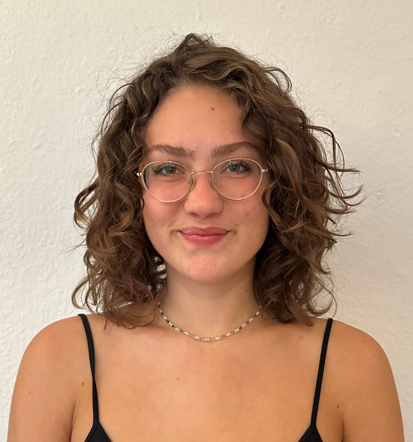 Lissy Malethan Porträt von Lissy Malethan: junge Frau mit Brille und lockigem dunklen Haar. Sie schaut lächelnd in die Kamera.