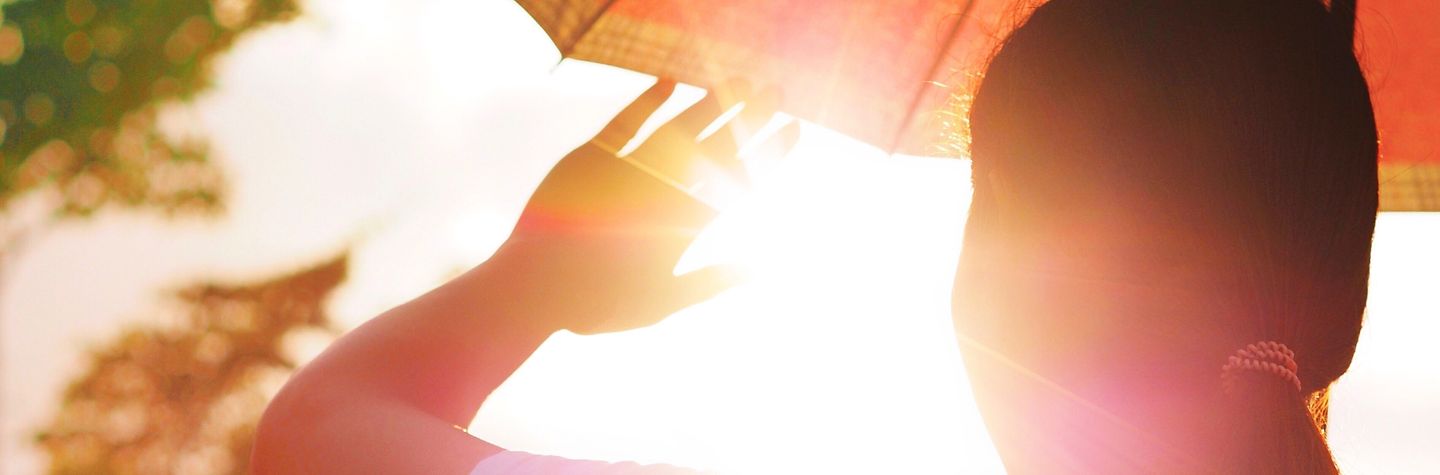 Junge Frau mit Schirm hält sich die Hand vors Gesicht gegen die strahlende Sonne.