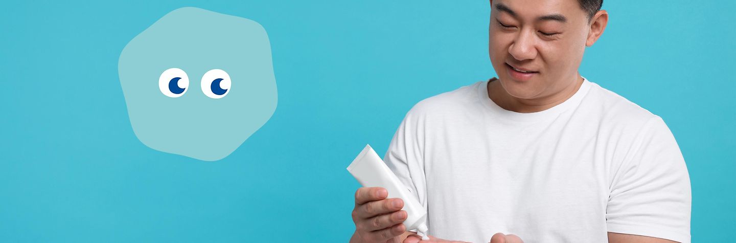 Junger Mann trägt mit Dermi Handcreme auf Junger Mann drückt Creme aus einer Tube auf seine Hand. Links von ihm schaut Dermi, eine hellblaue Hautzelle mit blauen Augen, dabei zu.