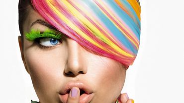 Bunte Haare Junge Frau mit bunt gefärbten Haaren hält sich den Zeigefinger vor die geschürzten Lippen.