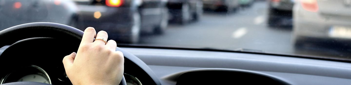 EIn Mann sitzt am Lenkrad eines Autos. Das Auto steht im Stau.