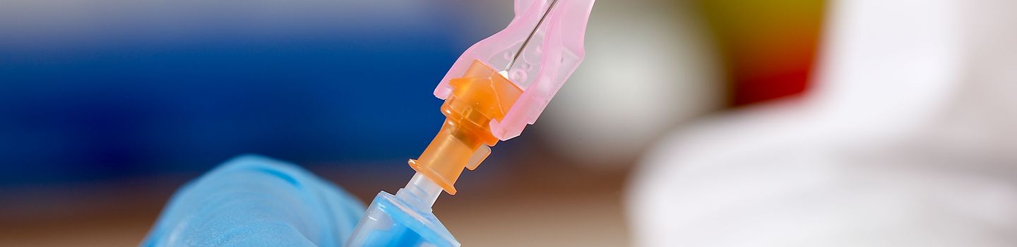 Detailaufnahme einer Hand, die eine Spritze mit Kanülenschutz hält