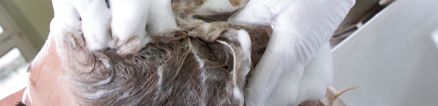 Für die Hände nur das Beste: Hautpflege im Salon Friseurin beim Haare waschen trägt Handschuhe mit Unterziehhandschuhen aus Baummwolle.