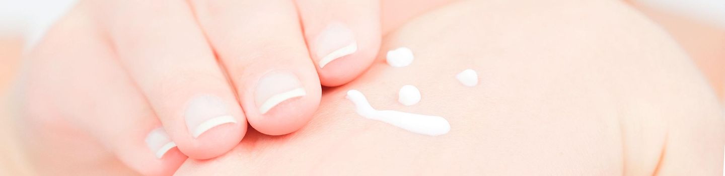 Die richtige Handpflege Nahaufnehme einer Hand. Mit Creme ist ein Smiley auf den Handrücken gemalt. Die zweite Hand mit gepflegten Fingernägeln kommt von links zum Verstreichen der Creme