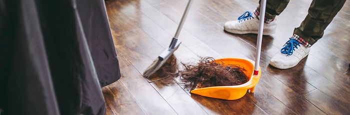 Haare auf dem Boden werden von einer Person in Sneakern zusammengekehrt