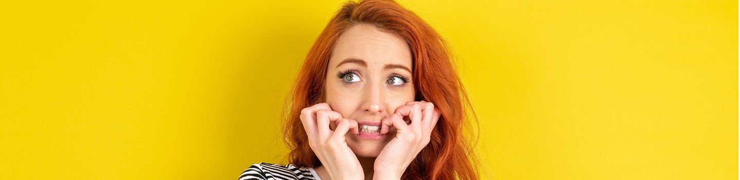 Junge rothaarige Frau hält sich grübelnd und sorgenvoll die Hände ans Gesicht