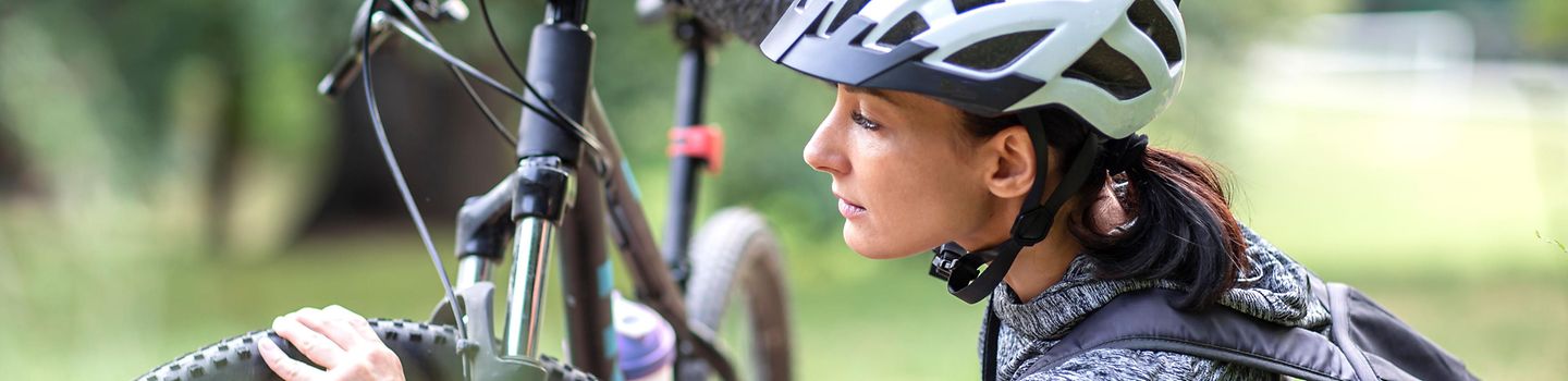 Fahrradcheck Frau mit Fahrradhelm prüft die Luft im Reifen an ihrem Fahrrad