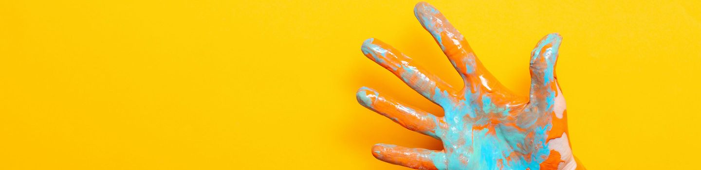 Hand mit bunter Farbe auf der Haut vor gelbem Hintergrund